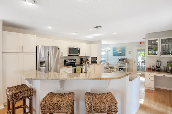 A modern kitchen with white cabinets, stainless steel appliances, a central island with bar stools, and a view to the dining area. - 5 BD, 3 bath, 200 Yards to Cocoa Beach (Cocoa Beach)