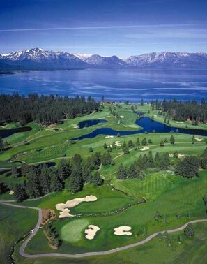 A golf course with a lake, forested areas, and mountains in the background.