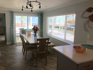 A dining area with a wooden table and chairs, a vase with flowers, and a window with blinds. - SPECTACULAR! PRIVATE POOL, OCEAN FRONT, & DOCK Sister house nextdoor VRBO#770357 (Marathon)