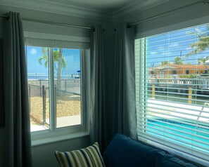 A room with a view of a beach and a pool, featuring a window with blinds and a striped pillow. - SPECTACULAR! PRIVATE POOL, OCEAN FRONT, & DOCK Sister house nextdoor VRBO#770357 (Marathon)