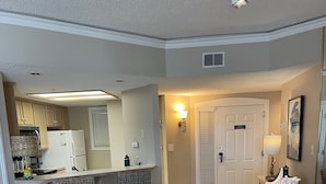 A compact kitchen with a refrigerator, stove, and microwave. There is a dining area with a glass table and wicker chairs. - Oceanfront - Very Comfortable - Windsor Court (Hilton Head Island)