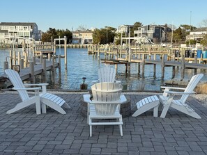 A waterfront patio with Adirondack chairs and a fire pit, overlooking a marina with docks and houses. - Bayfront  w/dock, fire pit, Beach Haven Park, LBI. Easy 2 blocks to beach (Long Beach Township)