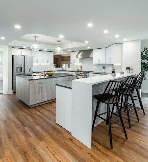 Una cocina moderna con una isla grande, piso de madera y taburetes de bar.