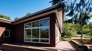 Una casa moderna con un amplio ventanal, una terraza de madera y vistas a árboles y un campo de golf.