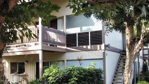 Ein modernes, zweistöckiges Gebäude mit Balkon, umgeben von üppiger Vegetation und einer Treppe, die zu einer oberen Ebene führt.