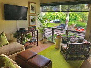 Relax in this inviting living room with a sofa, coffee table, and flat-screen TV, surrounded by lush views and potted plants.