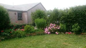 Una casa amb teulada inclinada, envoltada d'un jardí ben cuidat amb plantes i flors diverses.