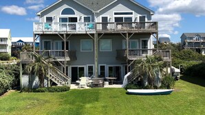 Una casa frente al mar de dos pisos con balcón, terraza cubierta y jardín.