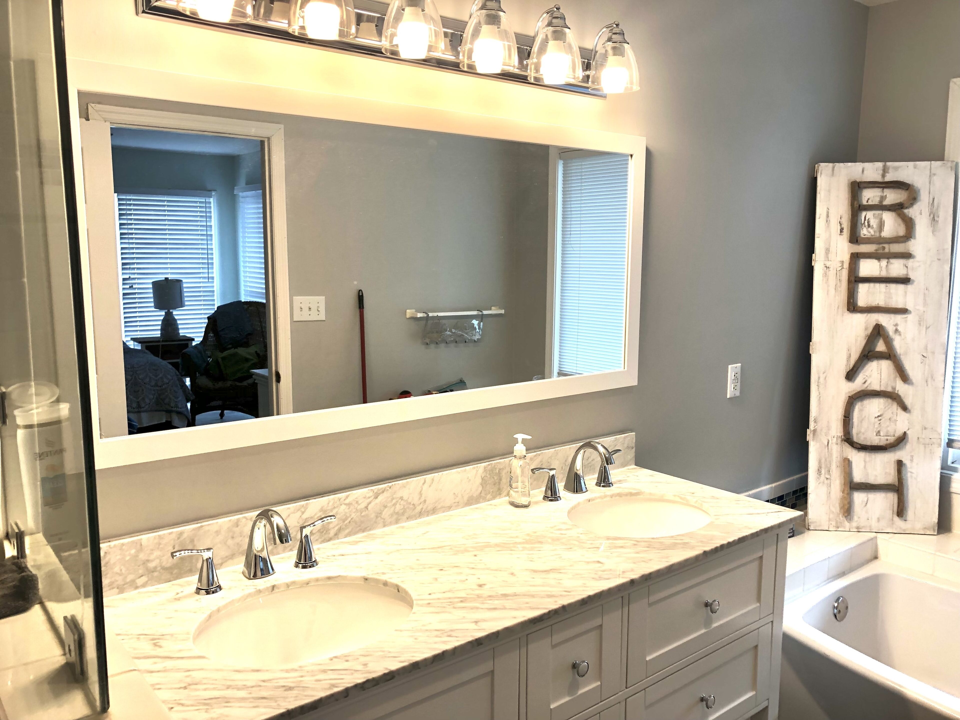 Une salle de bain avec un double lavabo, un grand miroir et un panneau indiquant « PLAGE ».