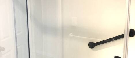 A glass-enclosed shower with a black towel rack and a black towel holder.
