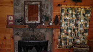 Interior de una cabaña de troncos con chimenea de piedra, paredes de madera, cortina acolchada y un cubo de metal.