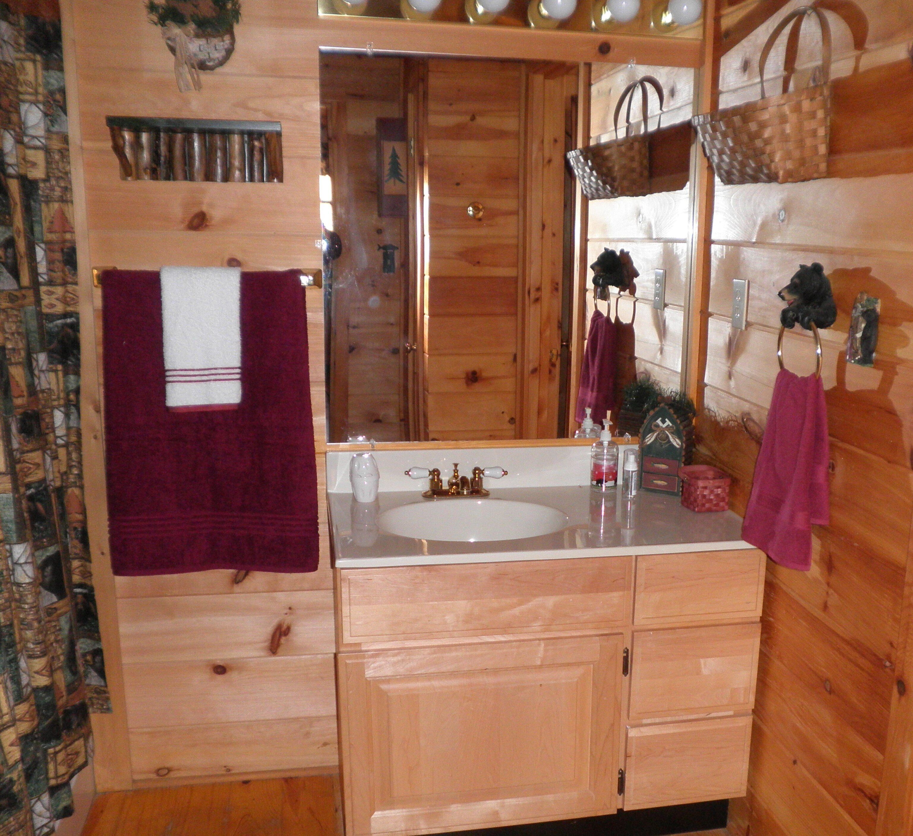 A wooden cabin bathroom with a large mirror, wooden cabinets, and a sink.