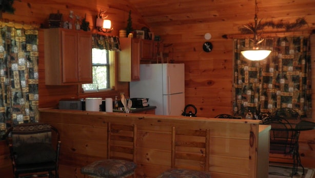 Interior de una cabaña de madera con cocina, asientos de bar y un ventilador de techo.