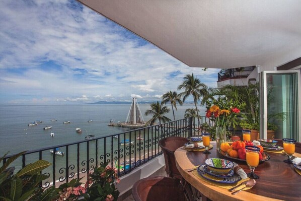Un balcon avec une table dressée pour le petit-déjeuner, donnant sur une étendue d’eau où l’on aperçoit des bateaux et un pont.