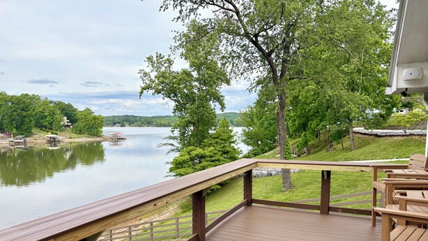 Une terrasse en bois avec une rambarde donnant sur un lac, entourée de verdure et bordée d’un quai.