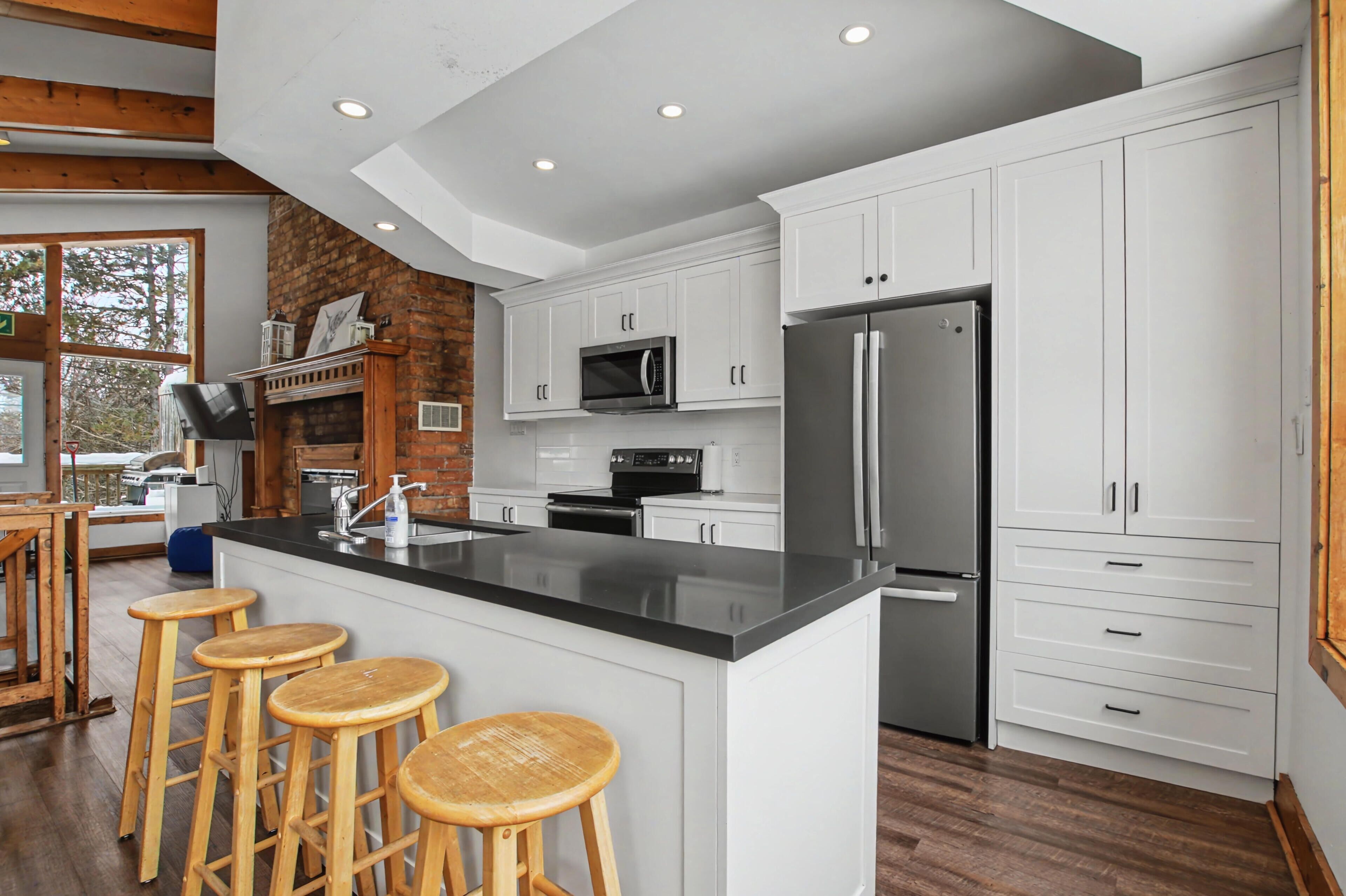 A modern kitchen with white cabinets, a stainless steel refrigerator, and a central island with stools.