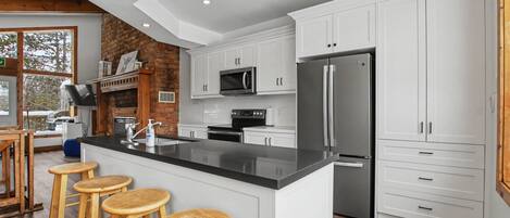 A modern kitchen with white cabinets, a stainless steel refrigerator, and a central island with stools.