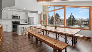A modern kitchen with white cabinets, stainless steel appliances, and a large wooden dining table with benches. - Birch View Chalet Blue Mountain (The Blue Mountains)