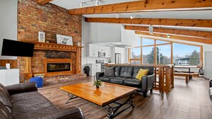 A spacious living room with a fireplace, leather sofas, a wooden coffee table, and large windows offering a view of the outdoors. - Birch View Chalet Blue Mountain (The Blue Mountains)