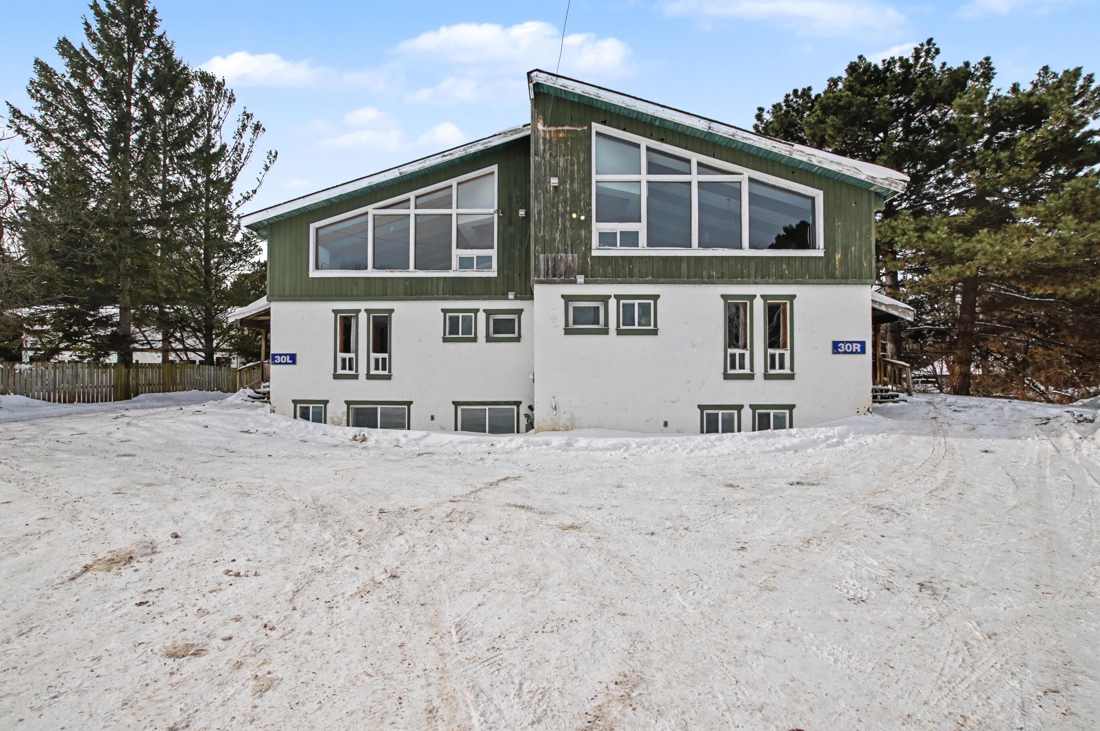 A two-story building with large windows and a green roof, surrounded by snow.