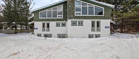 A two-story building with large windows and a green roof, surrounded by snow.