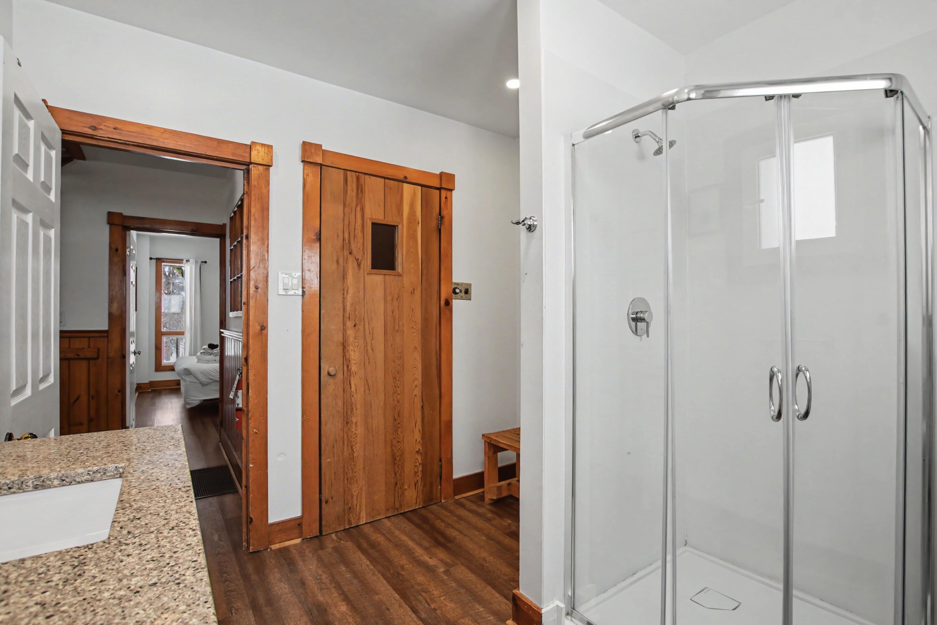 Un baño con cabina de ducha de vidrio, puerta de madera y encimera de granito.