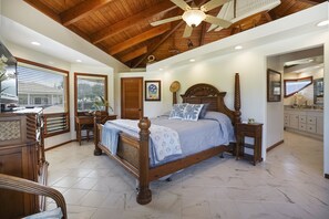 A bedroom with a wooden bed, a ceiling fan, and a view of the outside through large windows. - Waterfalls, Rainbows, Hot Tub, Golf, Tennis, Pool, Walk to Beach, Volleyball Crt (Princeville)