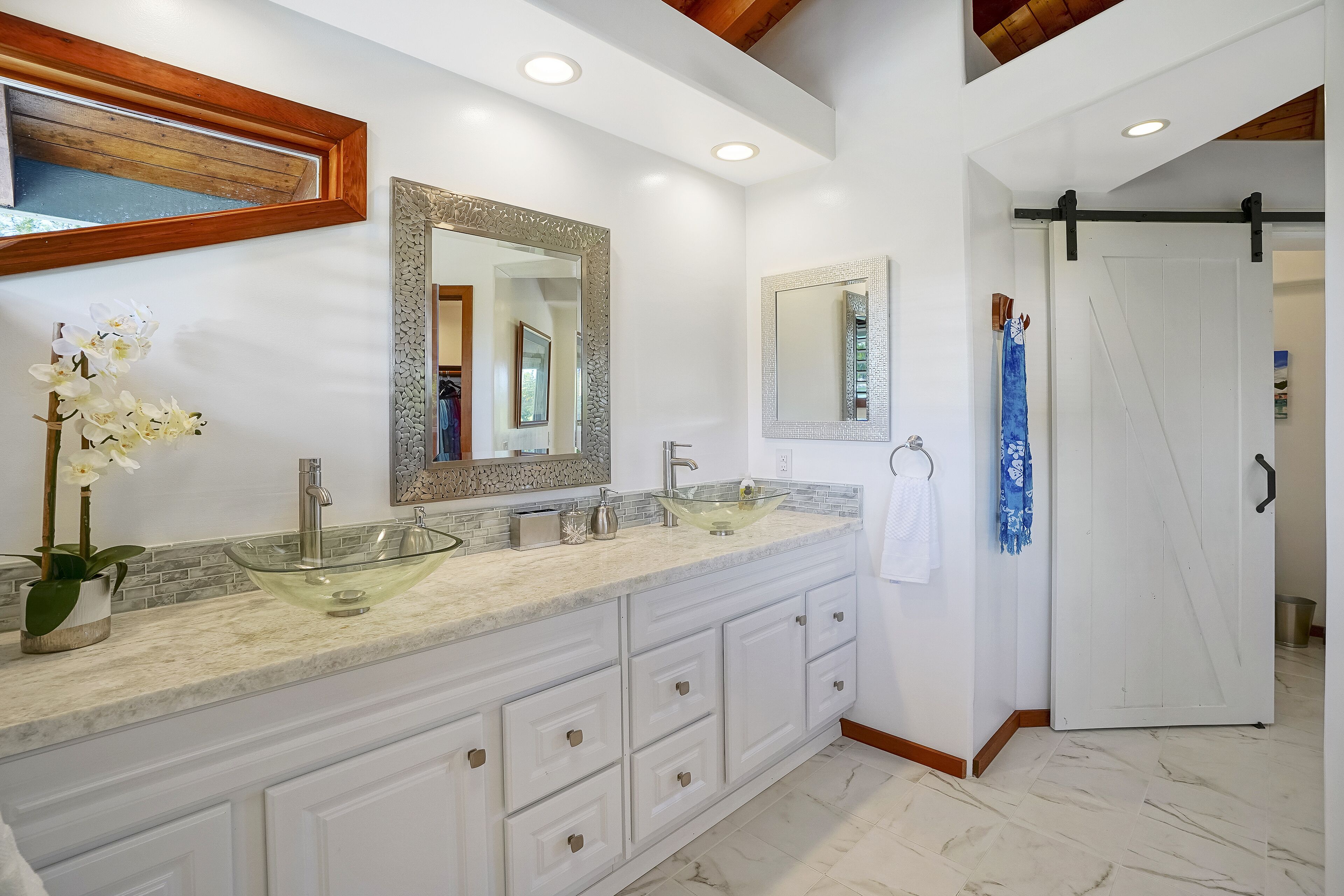 Un baño moderno con un lavabo grande de vidrio, muebles blancos y un espejo con marco de madera.