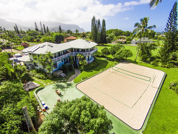 A large, two-story house with a balcony, surrounded by lush greenery and a tennis court. - Waterfalls, Rainbows, Hot Tub, Golf, Tennis, Pool, Walk to Beach, Volleyball Crt (Princeville)