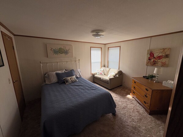 A bedroom with a bed, a nightstand, a dresser, and a window with blinds.