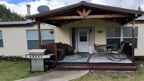 Una casa móvil con porche techado, una parrilla y mobiliario de exterior.