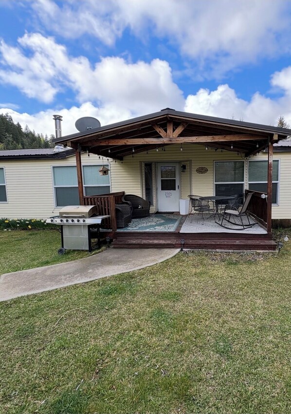 A mobile home with a covered porch, a grill, and outdoor seating.