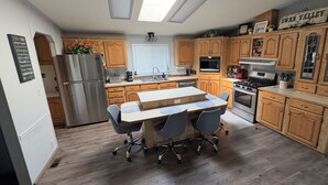 Una cocina con armarios de madera, una isla central con sillas, un refrigerador, una estufa y un microondas.