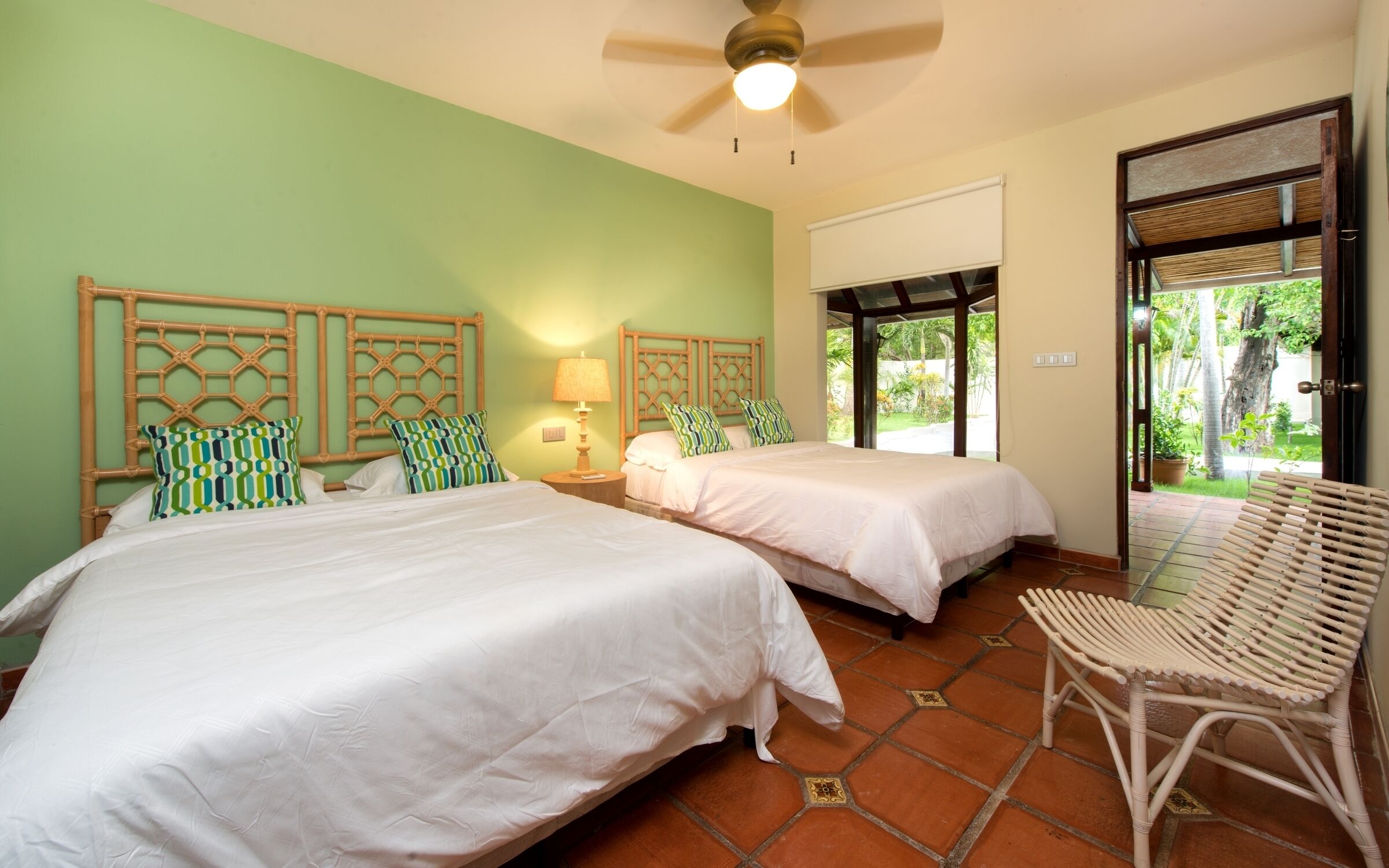 A hotel room with two beds, a ceiling fan, a chair, and a view of the outdoors.