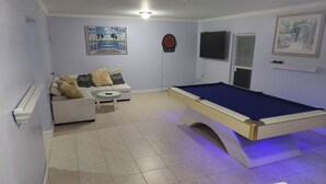A living room with a pool table, a sofa, and a television.