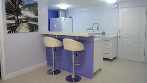 A kitchen with a bar area, two bar stools, a refrigerator, and a microwave.