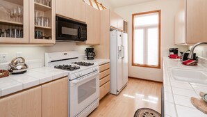 A modern kitchen with a gas stove, microwave, and refrigerator, wooden cabinets, and a window providing natural light. - Home Away From Home in Snowcreek V Resort (Mammoth Lakes)