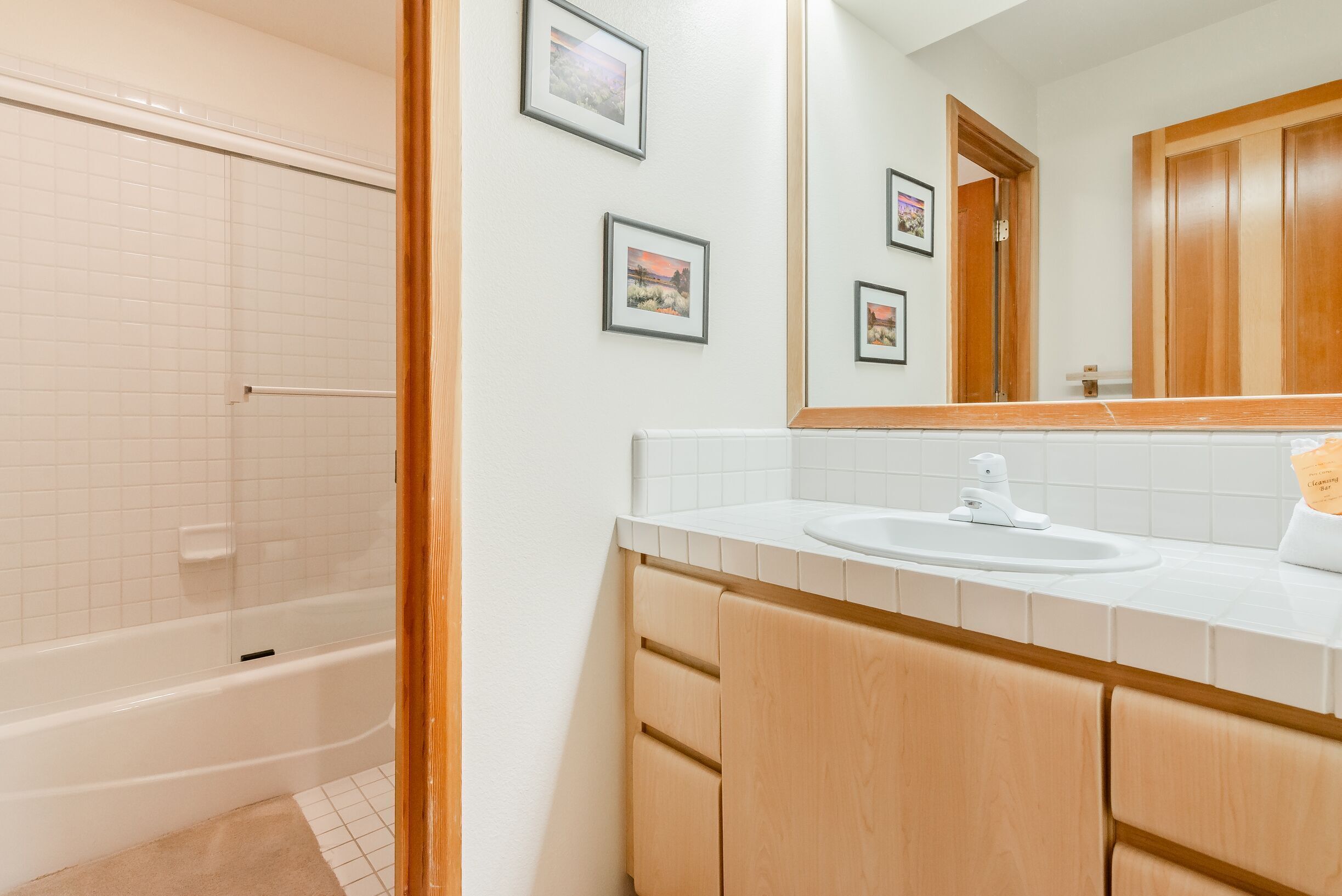 A bathroom with a bathtub, a sink, wooden cabinets, and a mirror.