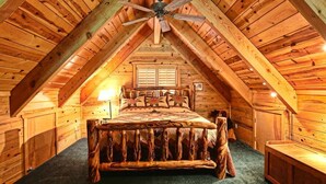 Un dormitorio tipo cabaña de madera con techo de madera, una cama con cabecera rústica y un ventilador de techo.