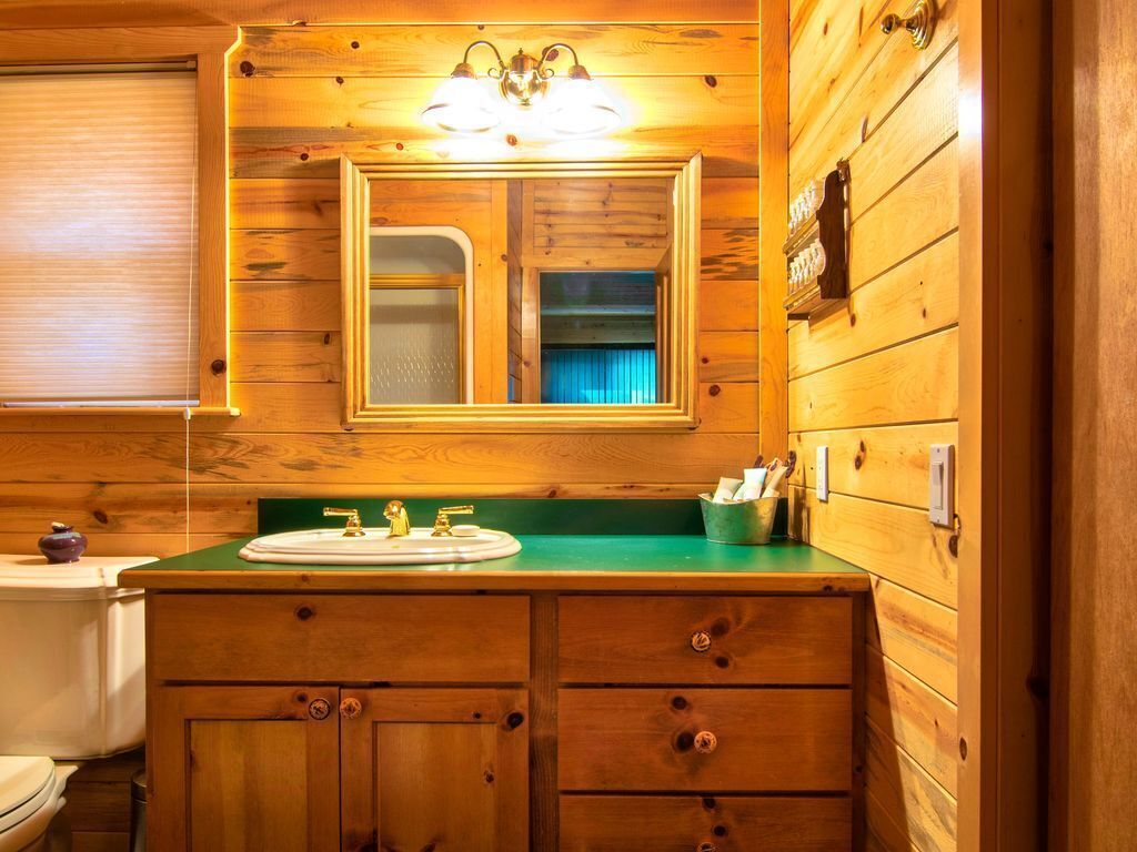 Un baño de cabaña de madera con lavamanos de encimera verde, armarios de madera y un espejo sobre el lavamanos.