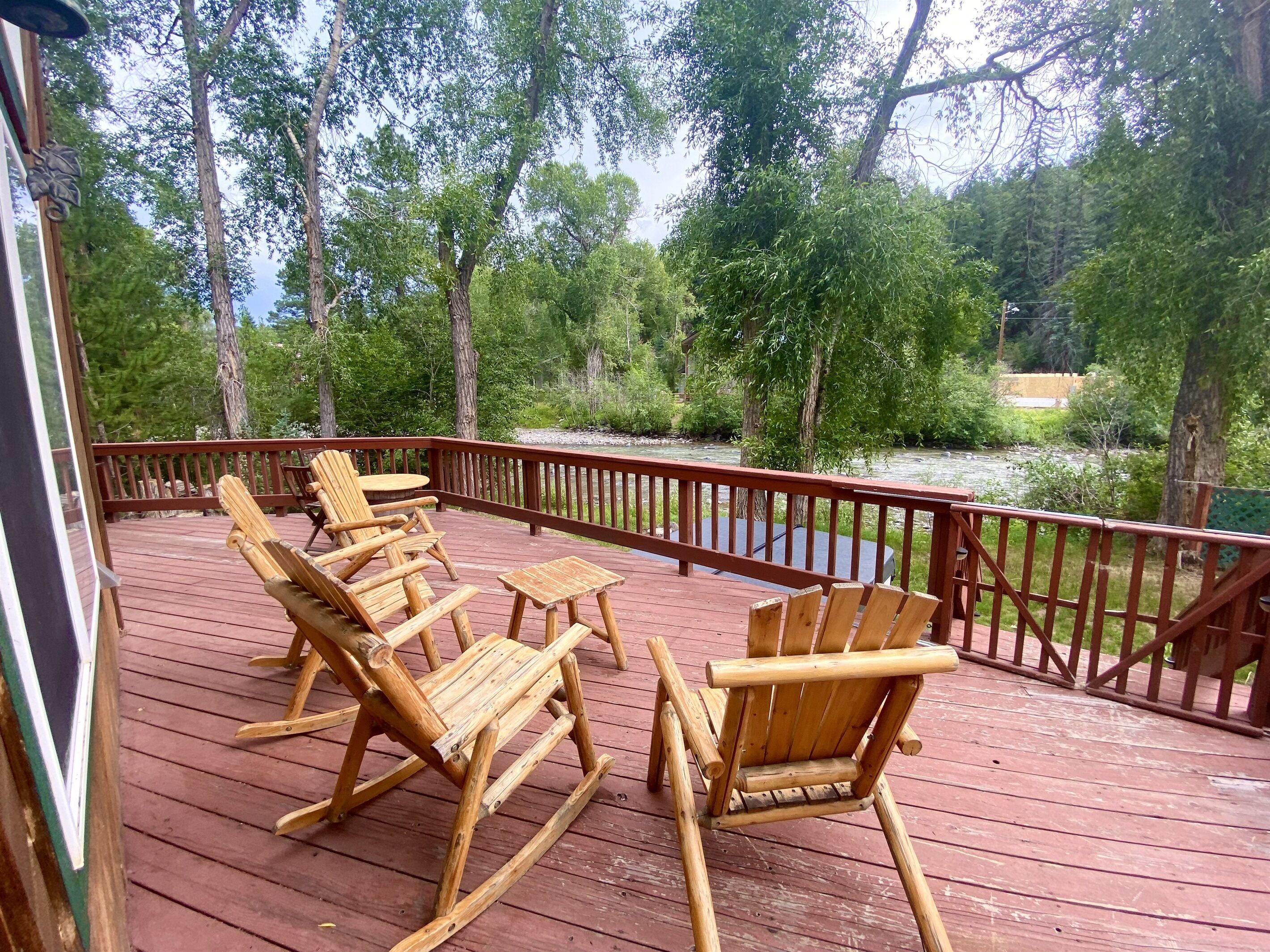 Une terrasse en bois avec des fauteuils à bascule et une table, offrant une vue sur une rivière et une zone boisée.