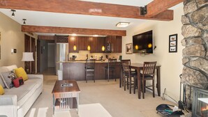 A spacious living area with a fireplace, a kitchen with wooden cabinets, and a dining area with chairs. - Lift One - Top floor remodeled one bedroom with view of Aspen Mountain (Aspen)