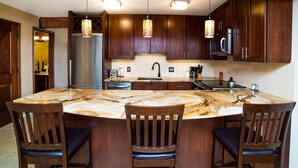 A modern kitchen with dark wood cabinets, a marble island with four chairs, stainless steel appliances, and pendant lighting. - Lift One - Top floor remodeled one bedroom with view of Aspen Mountain (Aspen)