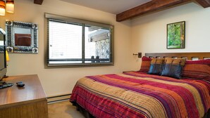 A bedroom with a large bed, a desk with a lamp, a window with blinds, and a framed picture on the wall. - Lift One - Top floor remodeled one bedroom with view of Aspen Mountain (Aspen)