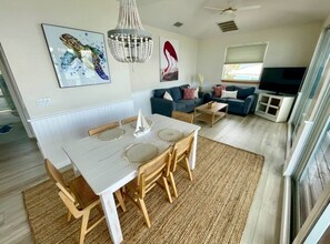 Ein modernes Wohnzimmer mit einem weißen Esstisch, blauen Sofas und einem Flachbildfernseher.
