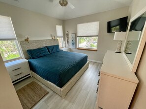 Ein Schlafzimmer mit Bett, Nachttischen, einem Schminktisch, einem Fernseher und Fenstern mit Jalousien.