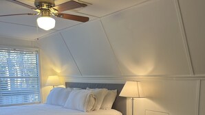 A bedroom with a bed, bedside lamps, a chair, a ceiling fan, and a window with blinds. - Sandy Beach, gorgeous sunsets, great front porch view! (Fairhope)