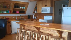 A modern kitchen with wooden cabinetry, a central island with stools, a microwave, and a refrigerator. - Sandy Beach, gorgeous sunsets, great front porch view! (Fairhope)