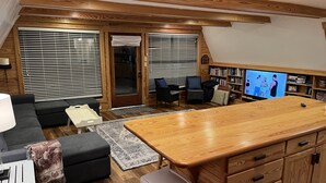 A cozy living area with a wooden ceiling, a sofa, a coffee table, a TV, and a bookshelf. - Sandy Beach, gorgeous sunsets, great front porch view! (Fairhope)