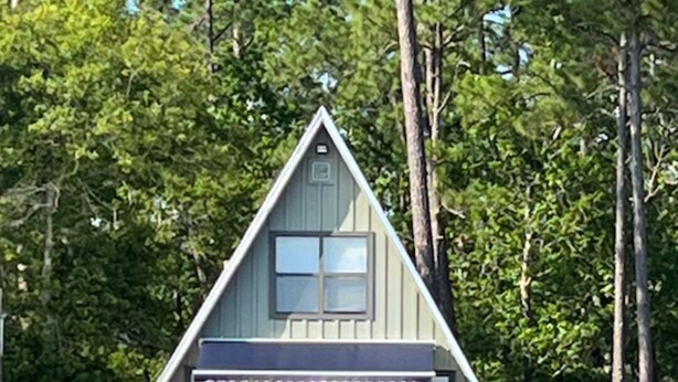 A cabin with a wooden deck, a covered outdoor seating area, and a dock leading to a body of water. - Sandy Beach, gorgeous sunsets, great front porch view! (Fairhope)